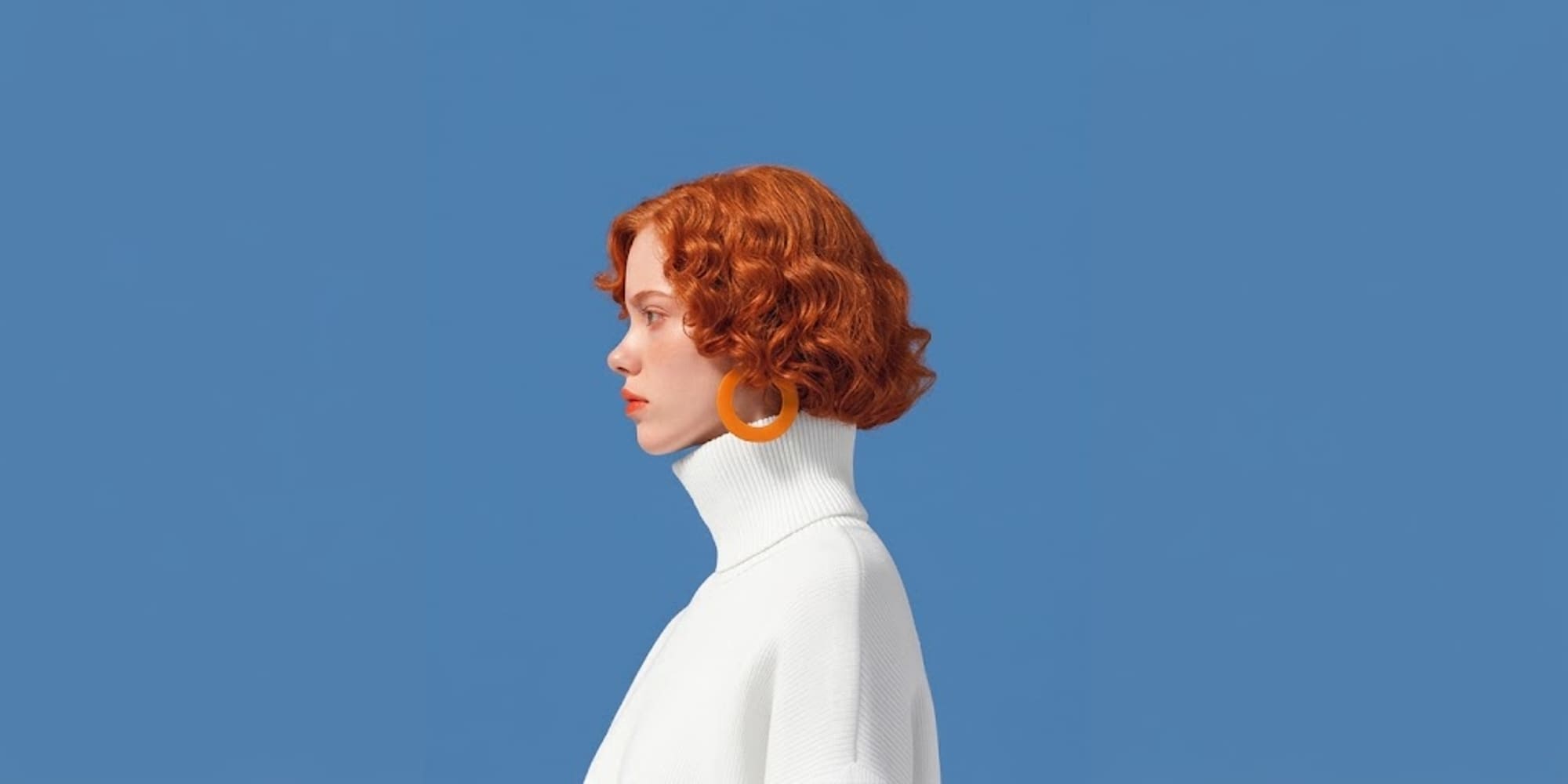 A woman in profile wearing a white roll-neck jumper and an orange hoop earring
